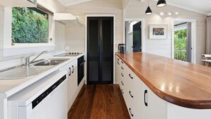 A modern kitchen with a wooden countertop, white cabinetry, and a view of greenery through a window. - Okere Tree House - Lakefront Retreat, Sleeps 8 (Okere Falls)