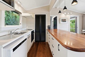A modern kitchen with a wooden countertop, white cabinetry, and a view of greenery through a window.