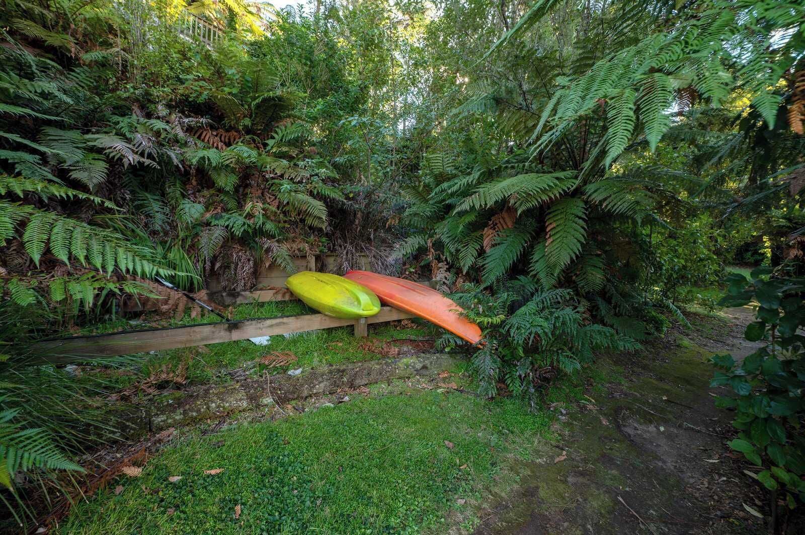 A natural setting with a wooden fence and two kayaks, surrounded by dense green foliage.