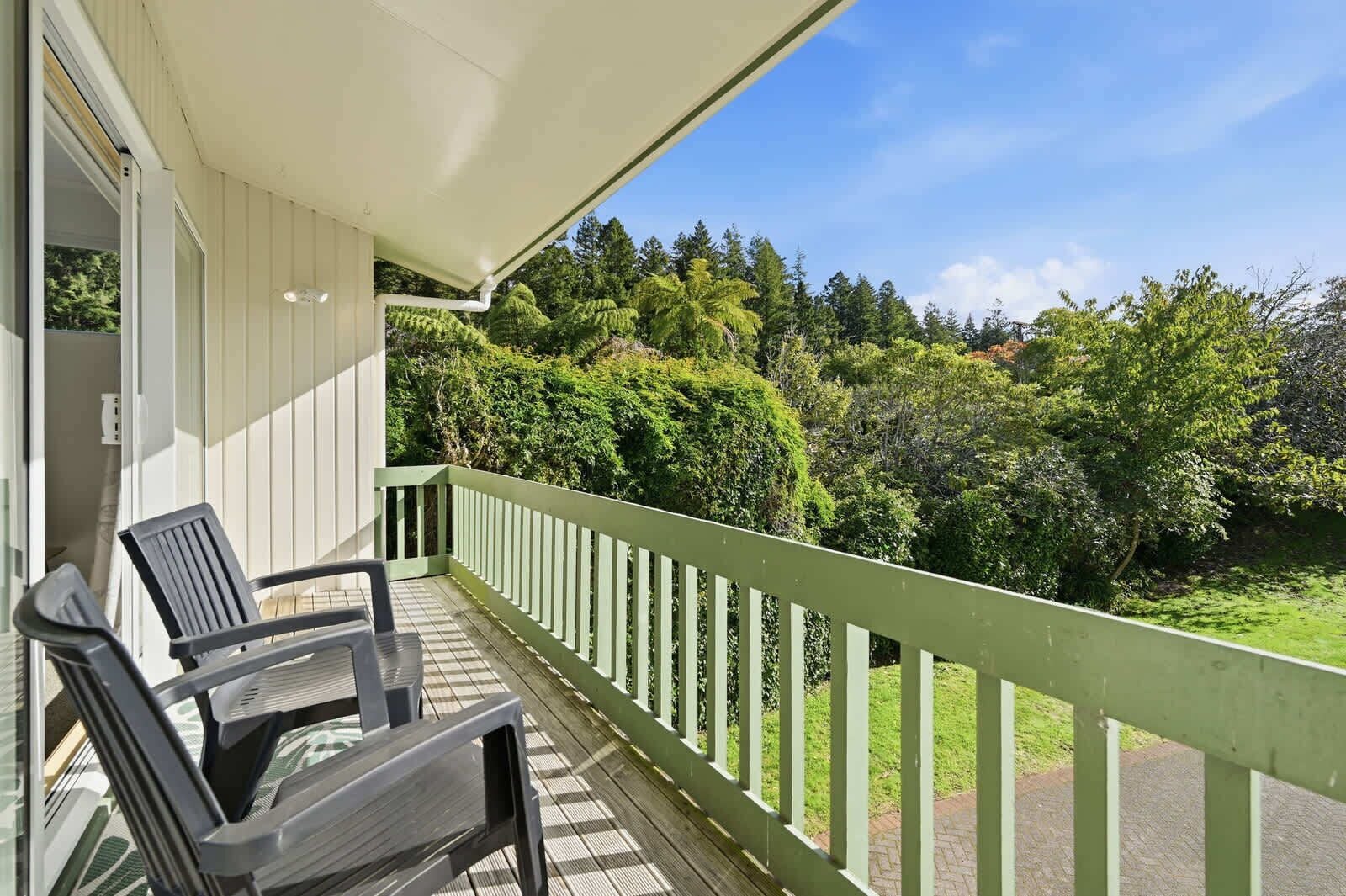 A balcony with two chairs, a white awning, and a view of dense greenery.