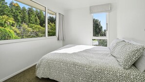 Un dormitorio con cama, dos ventanas y vista a zonas verdes.