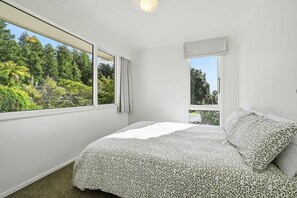 A bedroom with a bed, two windows, and a view of greenery.