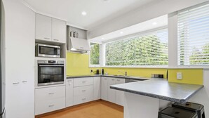 Una cocina moderna con armarios blancos, electrodomésticos de acero inoxidable, encimera de granito y una ventana con persianas.