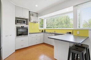 A modern kitchen with white cabinets, stainless steel appliances, a granite countertop, and a window with blinds. - Redwoods Edge - Forest Walk, Spa Pool, Sleeps 12 (Rotorua)