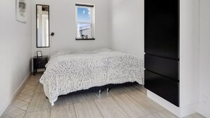 Un dormitorio con cama, cómoda, espejo, ventana y armario negro.