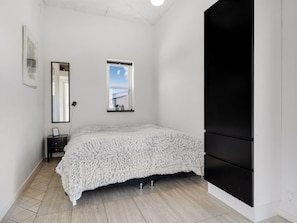 A bedroom with a bed, a dresser, a mirror, a window, and a black wardrobe.