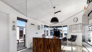 Una cocina moderna con una isla de madera, lámparas colgantes negras y vistas al exterior.