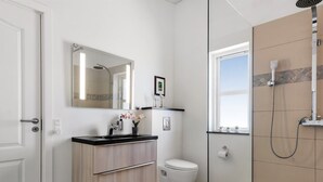 Un baño moderno con cabina de ducha de vidrio, inodoro, lavabo con espejo y un ventanal.