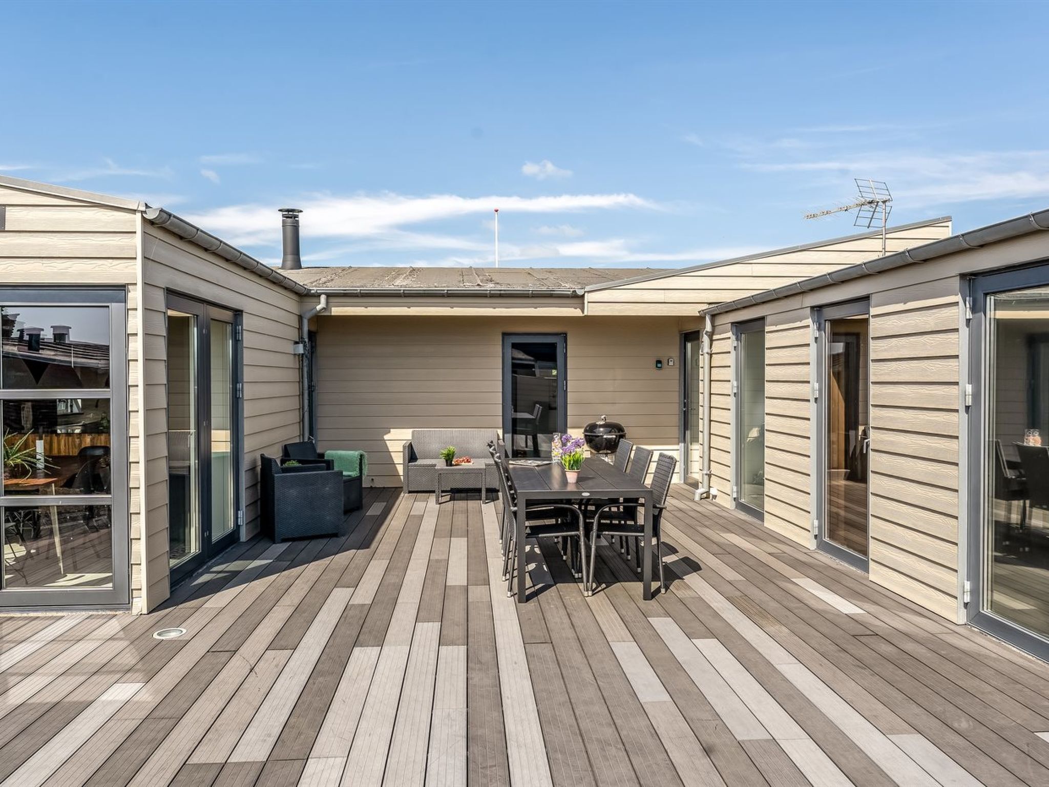 Eine überdachte Terrasse mit Esstisch und Stühlen, einem Grill und einer Schiebetür.