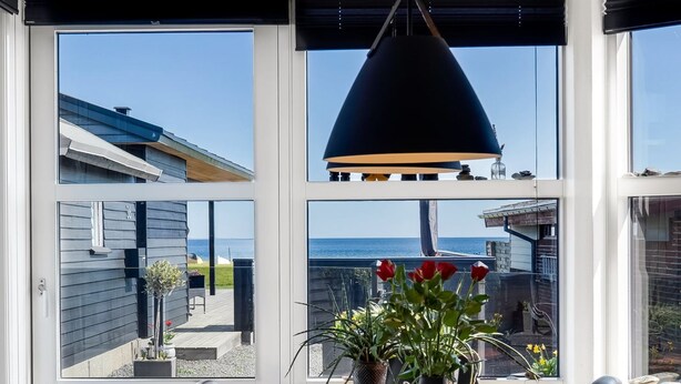 Un comedor con vista al mar, una mesa de madera, sillas negras y un colgador de luz.