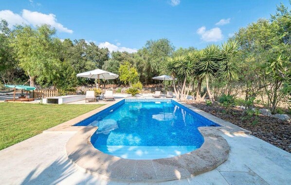 A rectangular swimming pool with a curved edge, surrounded by a concrete deck. There are lounge chairs and umbrellas in the background. - Nice home in Campos with private swimming pool, can be inside or outside (Campos)