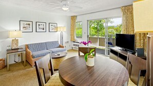 A living room with a sofa, a dining table with chairs, a TV, and a ceiling fan. - Kauai Condo-Pool View 1BR with Private Lanai A/C (Kapaʻa)