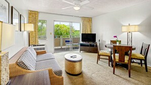 A living room with a sofa, a round coffee table, a TV, and a dining area with chairs and a table. - Kauai Condo-Pool View 1BR with Private Lanai A/C (Kapaʻa)