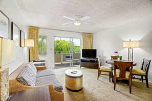 A living room with a sofa, a round coffee table, a TV, and a dining area with chairs and a table. - Lanai + Pool View Tropical Oasis, Plantation Hale (Kapaʻa)