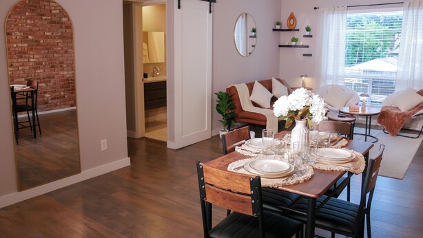 Uma área de refeições com mesa de madeira posta para quatro, um sofá e vista para o exterior.