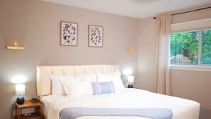 Cama bem arrumada com cabeceira, abajures laterais, mesa de cabeceira com luminária e quadros na parede.