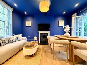 Ein Wohnzimmer mit blauer Wand, Kamin, Sofa, Couchtisch und Essbereich.