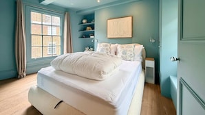 Ein Schlafzimmer mit einem Bett, einem Fenster, einem Regal mit Dekoration und einer Tür.