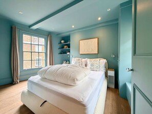 Ein Schlafzimmer mit einem Bett, einem Fenster, einem Regal mit Dekoration und einer Tür.