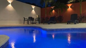 A swimming pool with chairs and a table, surrounded by a low wall and palm trees. - Beautiful King-Size Studio with Panoramic View (Playa del Carmen,)