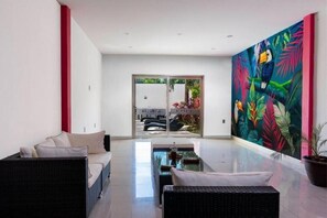 Un intérieur moderne avec un canapé, une table à manger et une grande fresque murale aux motifs tropicaux.