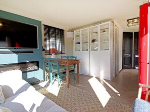 Una habitación con sofá, una mesa de comedor con sillas, televisor, lámpara y aparador con puertas de vidrio.