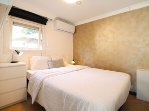 Un dormitorio con cama, mesitas de noche, ventana y equipo de aire acondicionado, y una pared con estampado.