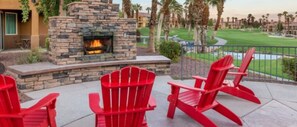 Eine Terrasse mit roten Adirondack-Stühlen, einem Steinkamin und Blick auf einen Golfplatz.