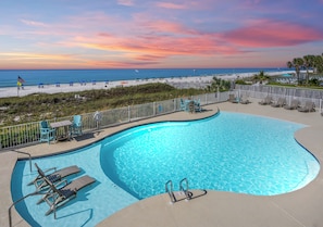 A swimming pool with lounge chairs, a table, and a view of the beach and ocean at sunset. - The Enclave 502 | Beachfront | Private Balcony | Indoor Pool | My Beach Getaways (Orange Beach)