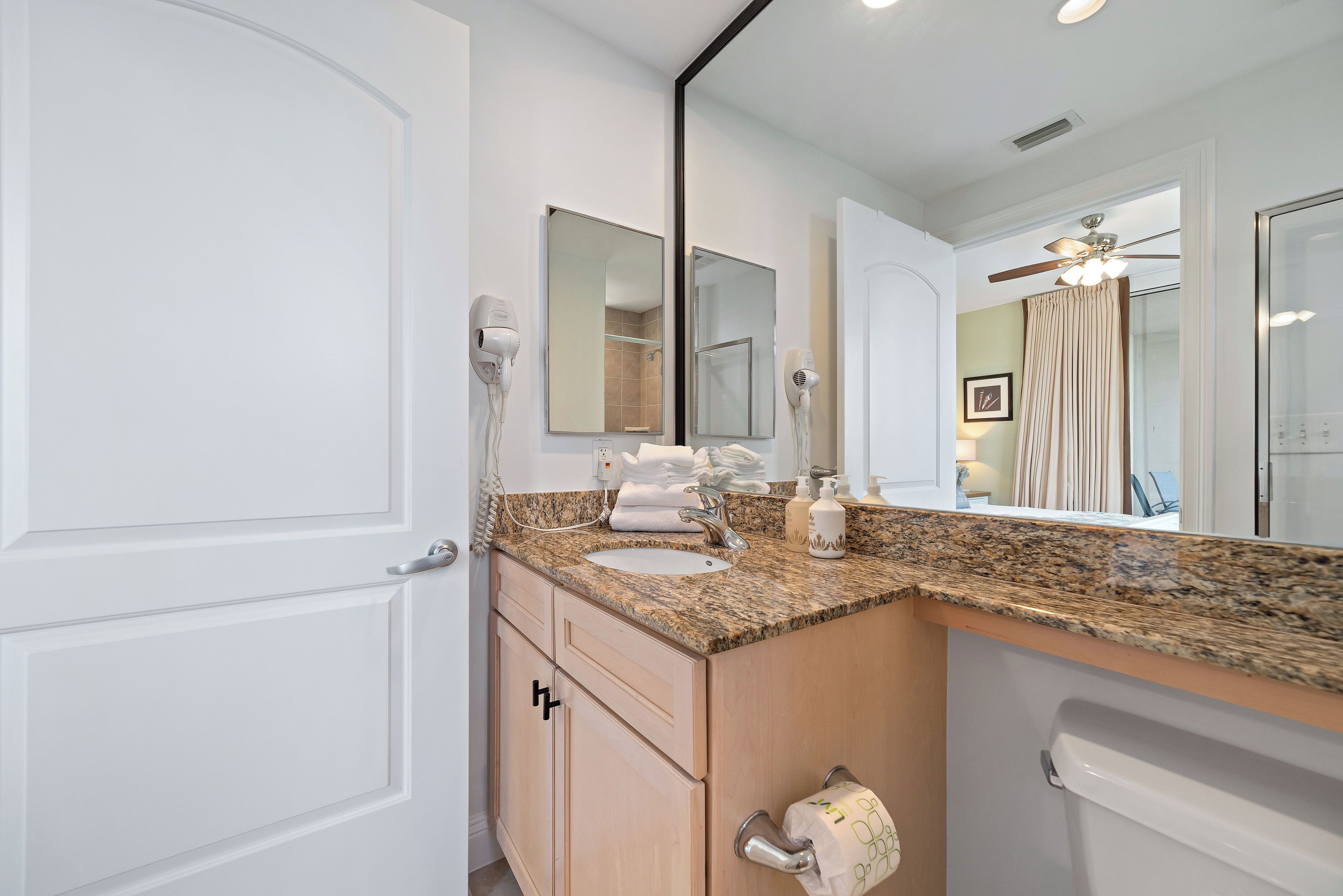 A bathroom with a granite countertop, a sink, a mirror, and a toilet.