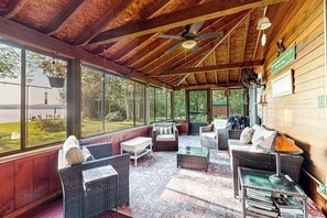 Ein überdachter Außenbereich mit Korbmöbeln, großen Fenstern und einem Deckenventilator.