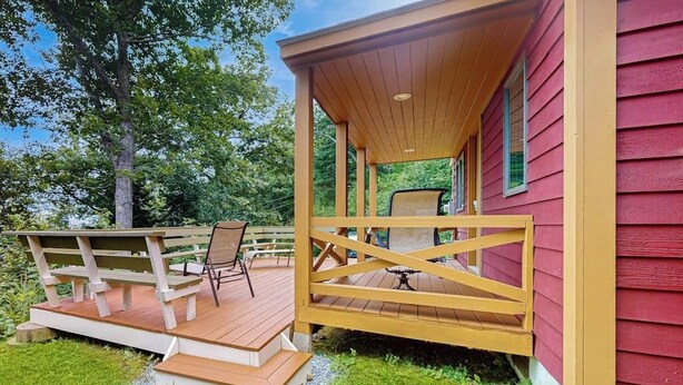 A wooden deck with a bench and a table, a covered porch, and a red building.