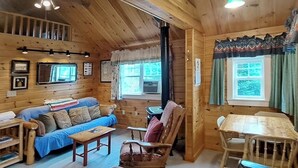 A wooden cabin interior with a sofa, a dining table, a chair, and a ceiling fan. - Lakefront cottage with full kitchen, firepit, gas grill, Wifi, a/c (Greenville)