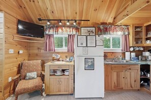 A wooden cabin interior with a kitchen area, a dining table, and a television mounted on the wall.