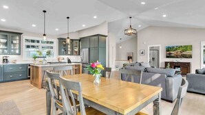 Una cocina amplia con electrodomésticos modernos, un comedor con mesa y sillas de madera, y una sala de estar con sofá gris.