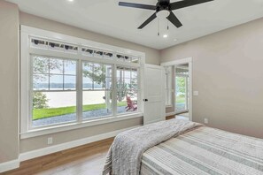 A bedroom with a large window, a ceiling fan, and a bed. - Elegant lakefront home near Bar Harbor & Acadia with modern kitchen, lake views (Orland)