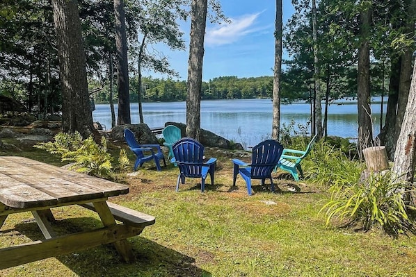Kaunis paikka järven rannalla, jossa on piknikpöytä ja Adirondack-tyyliset puutarhatuolit.