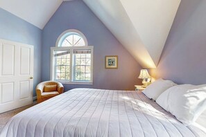 Ein Schlafzimmer mit einem großen Bett, einem Fenster mit Blick, einem Sessel und einem Nachttisch mit Lampe.
