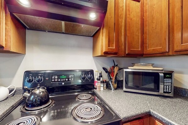 Una cucina con fornello, microonde, pensili in legno e bollitore.