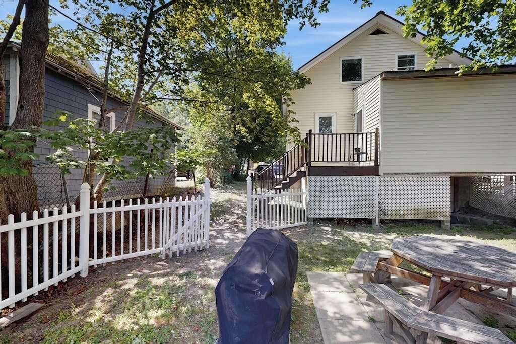 Een achtertuin met een overdekte barbecue, een picknicktafel, een wit hek en een huis met een balkon.