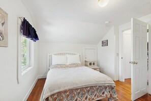 Une chambre à coucher comprenant un lit, une table de chevet, une fenêtre avec des rideaux, une porte et un luminaire fixé au mur.
