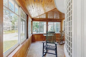 A room with large windows, wooden walls, a rocking chair, and a chair.