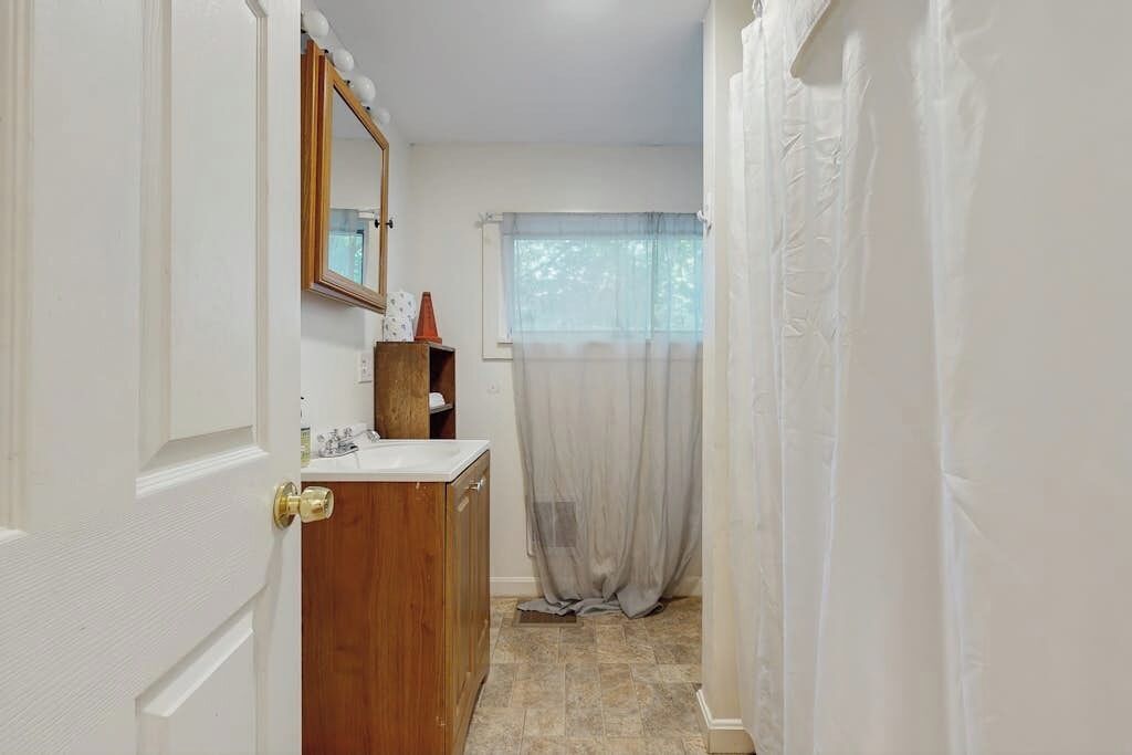 A narrow bathroom with a wooden cabinet, a mirror, and a shower curtain.