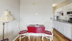 Une cuisine de taille réduite avec des meubles blancs, une table rouge et deux chaises blanches.