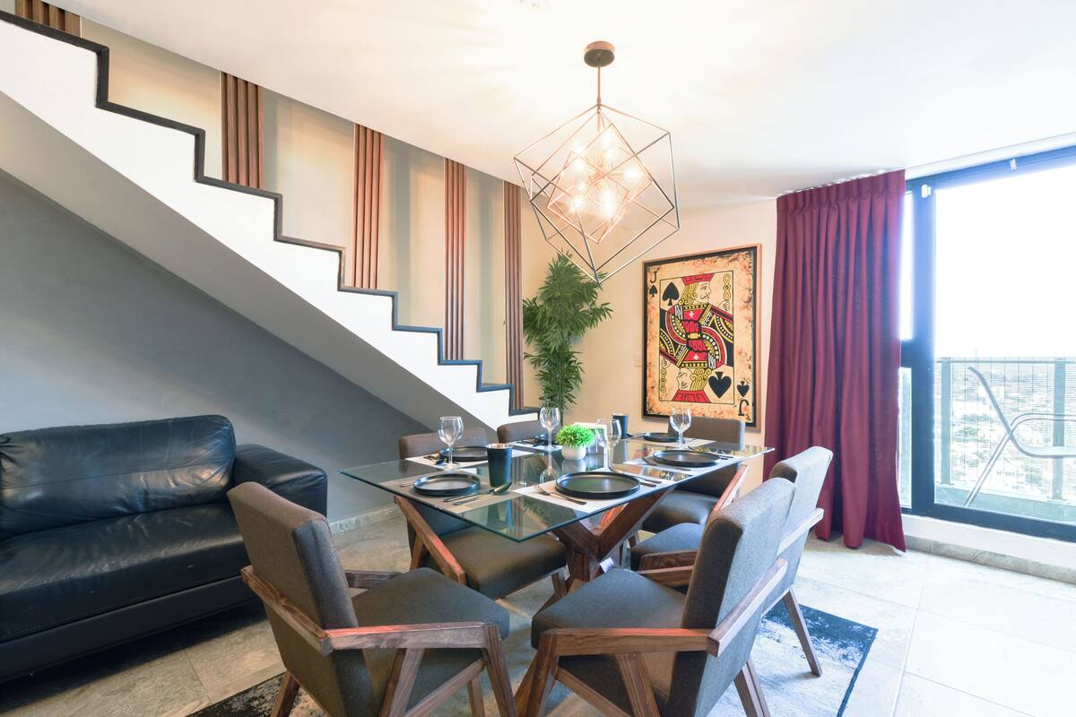 A modern dining area with a glass table, chairs, and a staircase.