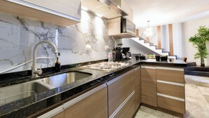 A modern kitchen with a marble backsplash, stainless steel sink, wooden cabinets, and a built-in stove. - El Semillero (Monterrey)
