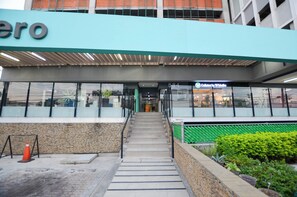 A building entrance with a staircase leading to a glass door, a sign above reading 'Cafeteria in Warehouse,' and a stone wall to the left. - El Semillero (Monterrey)