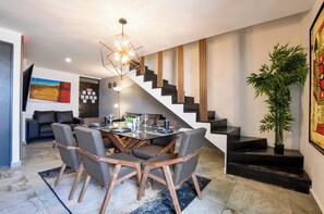 A modern dining area with a wooden table, chairs, and a geometric light fixture. - El Semillero (Monterrey)