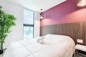 A modern hotel room with a large bed, a potted plant, a view of the city, and a wooden panel wall. - El Semillero (Monterrey)