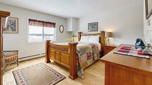A bedroom with a wooden bed, a bedside table, a nightstand, a window with a view, and a chair.